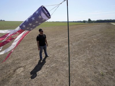 Hay farmer Milan Adams stands in a dry hay field near a wind sock, left, in Exeter, R.I., Tuesday, Aug. 9, 2022. Adams said in prior years it rained in the spring. This year, he said, the dryness started in March, and April was so dry he was nervous about his first cut of hay. (AP Photo/Steven Senne)