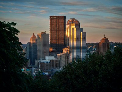 The Pittsburgh skyline is shown in the evening through trees